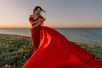 woman red dress standing grassy hillside. The sun is setting in the background, casting a warm glow over the scene. The woman is enjoying the beautiful view and the peaceful atmosphere.