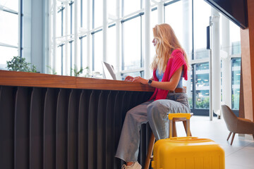 Female blogger and traveler, sitting at a table in an airport cafe, reads an article about travel