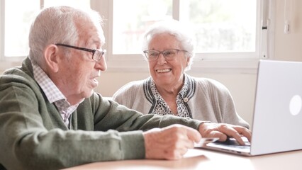 Happy senior couple chatting online using laptop at nursing home