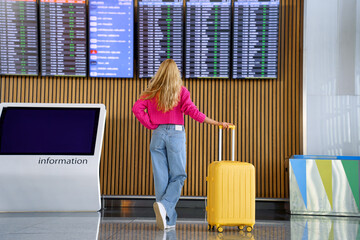 woman with luggage looks at airplane schedule board at airport