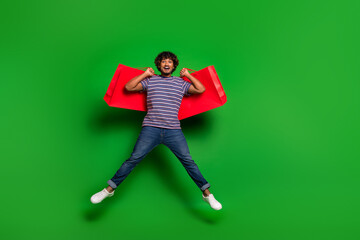Photo of young latin curly funny man student in striped t shirt jumping with bargains packages from...