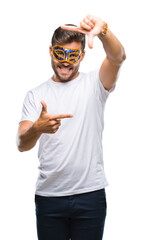 Young handsome man wearing carnival mask over isolated background smiling making frame with hands and fingers with happy face. Creativity and photography concept.