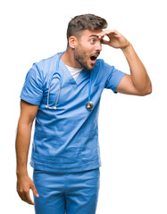 Fototapeta premium Young handsome doctor surgeon man over isolated background very happy and smiling looking far away with hand over head. Searching concept.