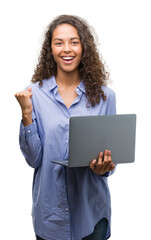 Young hispanic woman holding computer laptop screaming proud and celebrating victory and success very excited, cheering emotion