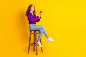 Full body photo of pretty young girl sit chair hold device wear trendy violet outfit isolated on yellow color background