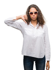 Young hispanic woman wearing sunglasses with angry face, negative sign showing dislike with thumbs down, rejection concept