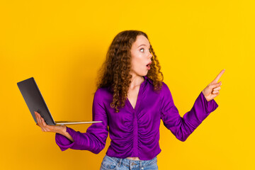 Photo portrait of pretty young girl hold laptop point look scared empty space wear trendy violet outfit isolated on yellow color background - obrazy, fototapety, plakaty