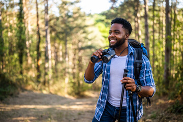 Young man enjoys using binoculars and hiking in nature.	