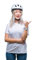 Young blonde woman wearing cyclist security helmet over isolated background smiling with happy face looking and pointing to the side with thumb up.