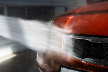 Close-up of a jet of water being sprayed onto a car from a gun in a car wash bay. The car is...