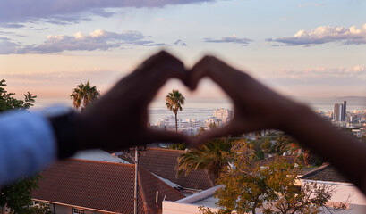 Hands, couple and heart shape in city on rooftop with sky, clouds and trees with symbol for connection. People, kindness and care with sign, emoji or icon with buildings in neighborhood on balcony