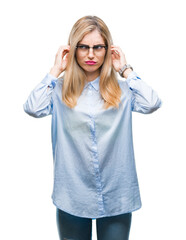 Young beautiful blonde business woman wearing glasses over isolated background covering ears with fingers with annoyed expression for the noise of loud music. Deaf concept.