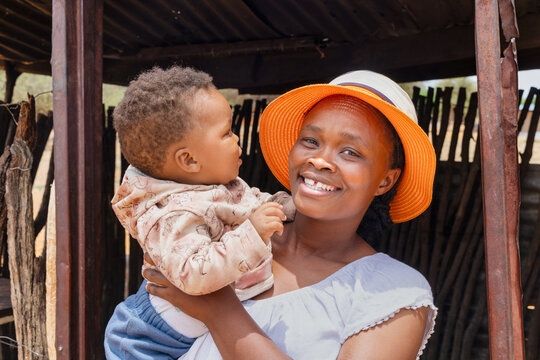 village african mother and baby standing at the entrance of the shack, township village in south africa