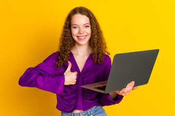 Photo portrait of lovely young lady hold netbook thumb up dressed stylish violet garment isolated on yellow color background