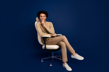 Full body photo of attractive young man sit armchair minded dressed stylish beige clothes isolated on dark blue color background