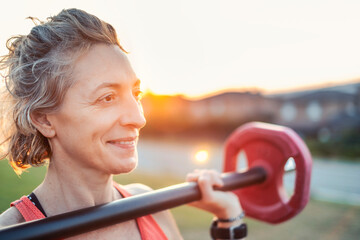 A woman is holding a red weight bar and smiling.