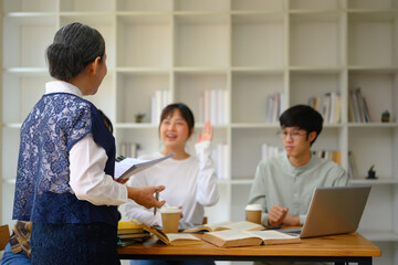 Positive mature lecturer talking to group of students during class. Education concept