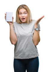 Obraz premium Young caucasian woman holding blank notebook over isolated background very happy and excited, winner expression celebrating victory screaming with big smile and raised hands