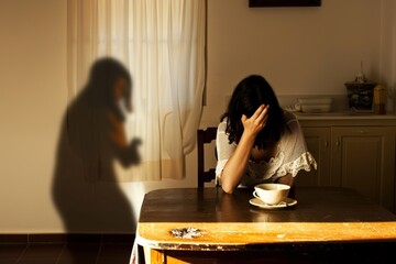 Powerful image captures a woman sitting at a table, her face hidden in her hand, while the looming shadow portrays the burden of depression