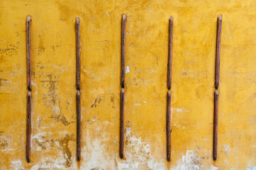 The surface of an old yellow-painted wall with numerous scratches, gouges and white stains, held...