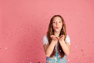 Photo of cute young girl blow air confetti wear dress isolated on pink color background