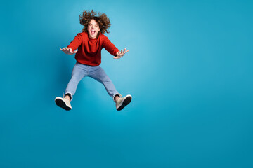 Full length photo of cheerful positive guy dressed red pullover jumping high emtpy space isolated blue color background
