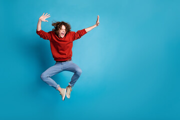 Obraz premium Full length photo of carefree positive guy dressed red pullover jumping high emtpy space isolated blue color background