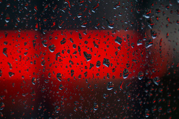 gocce di pioggia sul vetro di una finestra e sullo sfondo un neon rosso di un'insegna di un bar,...