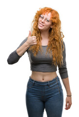 Young redhead woman doing happy thumbs up gesture with hand. Approving expression looking at the camera with showing success.