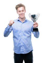 Young handsome blond man holding a trophy screaming proud and celebrating victory and success very excited, cheering emotion