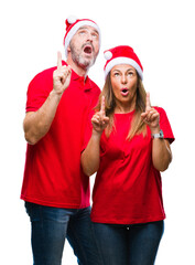 Middle age hispanic couple wearing christmas hat over isolated background amazed and surprised looking up and pointing with fingers and raised arms.