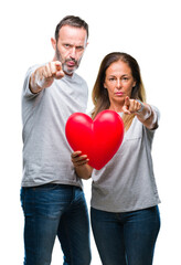 Middle age hispanic casual couple in love holding red heart over isolated background pointing with...