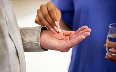 Obraz premium Hands, elderly patient and nurse with pills as medicine, antibiotics and water glass in homecare. Healthcare, Mature man and caregiver for helping, assistance and medication for old person wellness