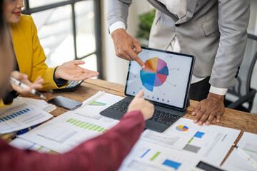A group of people are looking at a pie chart on a laptop. The man pointing at the chart is explaining something to the others