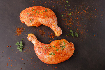 Marinated in tomato sauce with herbs and pepper raw legs of chicken on brown stone background. ...
