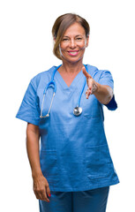 Middle age senior nurse doctor woman over isolated background smiling friendly offering handshake as greeting and welcoming. Successful business.
