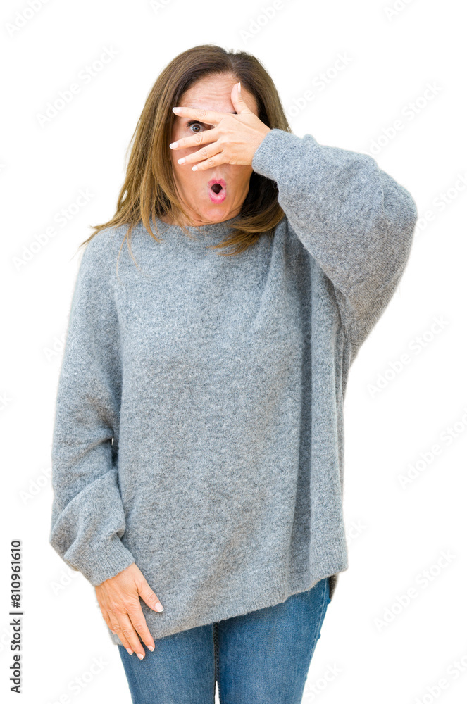 Poster Beautiful middle age woman wearing winter sweater over isolated background peeking in shock covering face and eyes with hand, looking through fingers with embarrassed expression.