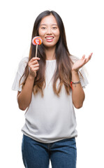 Young asian woman eating lollipop candy over isolated background very happy and excited, winner expression celebrating victory screaming with big smile and raised hands