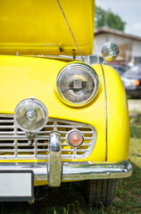 Front view of a yellow vintage car headlights. Classic car. Open hood.	