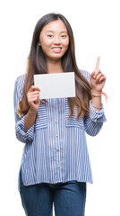 Young asian woman holding blank card over isolated background surprised with an idea or question pointing finger with happy face, number one