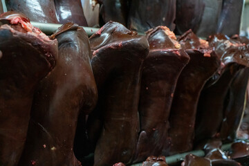 Lots of cattle livers are hung side by side with hooks.