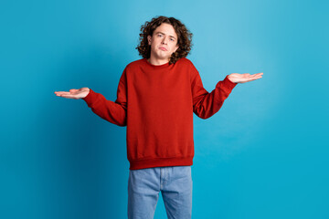 Photo of funky doubtful guy dressed red pullover shrugging shoulders emtpy space isolated blue...