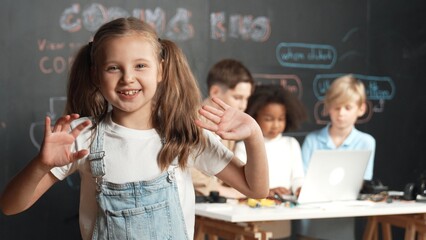 Girl smile and wave to camera while friend working or learning engineering code or prompt in STEM...