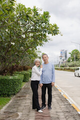 Happy Asian senior couple walking together on a tropical forest path Retired old man and woman...