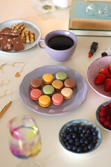 Plate of pastel macarons, cookies and chocolate, cup of tea of coffee, glass of bubble water,...