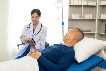Obraz premium Beautiful nurse doctor feels happy while talking and supporting an elderly male nursing home patient lying in bed.