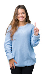 Young beautiful brunette woman wearing blue winter sweater over isolated background showing and pointing up with finger number one while smiling confident and happy.