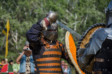 Battle of warriors tournament. Armed members of history club in knight armor demonstrating fighting...