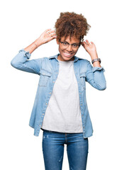 Beautiful young african american woman wearing glasses over isolated background Smiling pulling ears with fingers, funny gesture. Audition problem