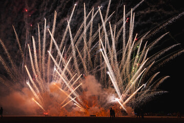 Vibrant fireworks illuminate the desert night sky in a captivating display of white, yellow, and...